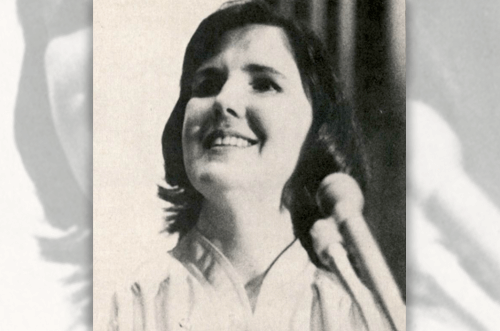 Black and white photo of blind woman looking up while standing in front of microphone